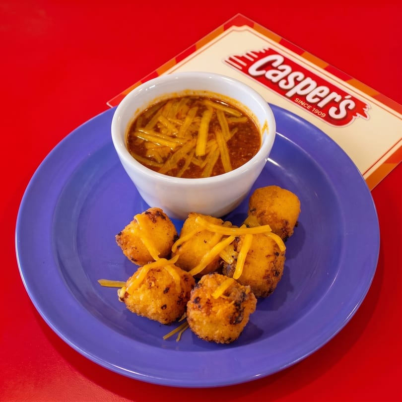 Casper's chili with shredded cheese and a side of fried cheese curds on a purple plate.