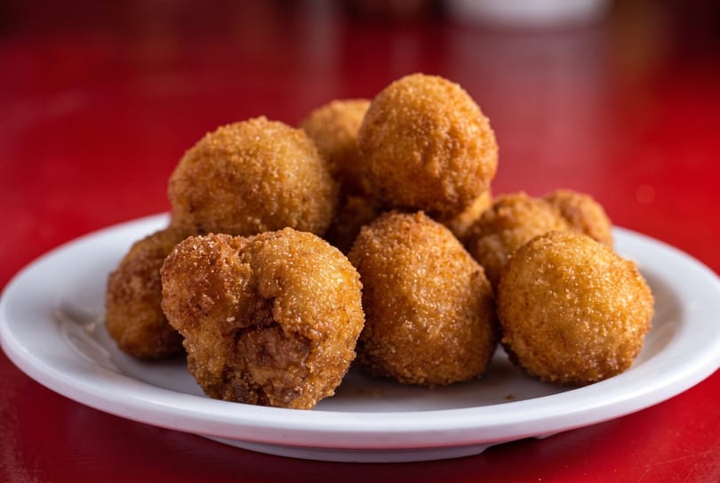 A white plate filled with golden-brown, breaded, fried croquettes on a vibrant red surface.