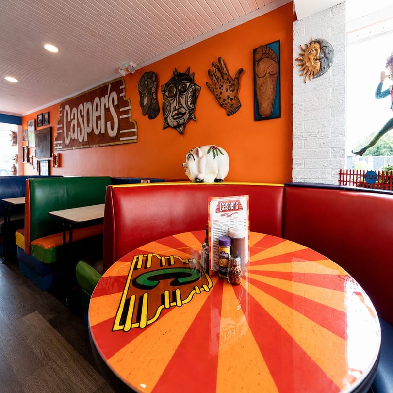 Colorful interior of Casper's restaurant with red and green booths, orange walls, and a striped table.